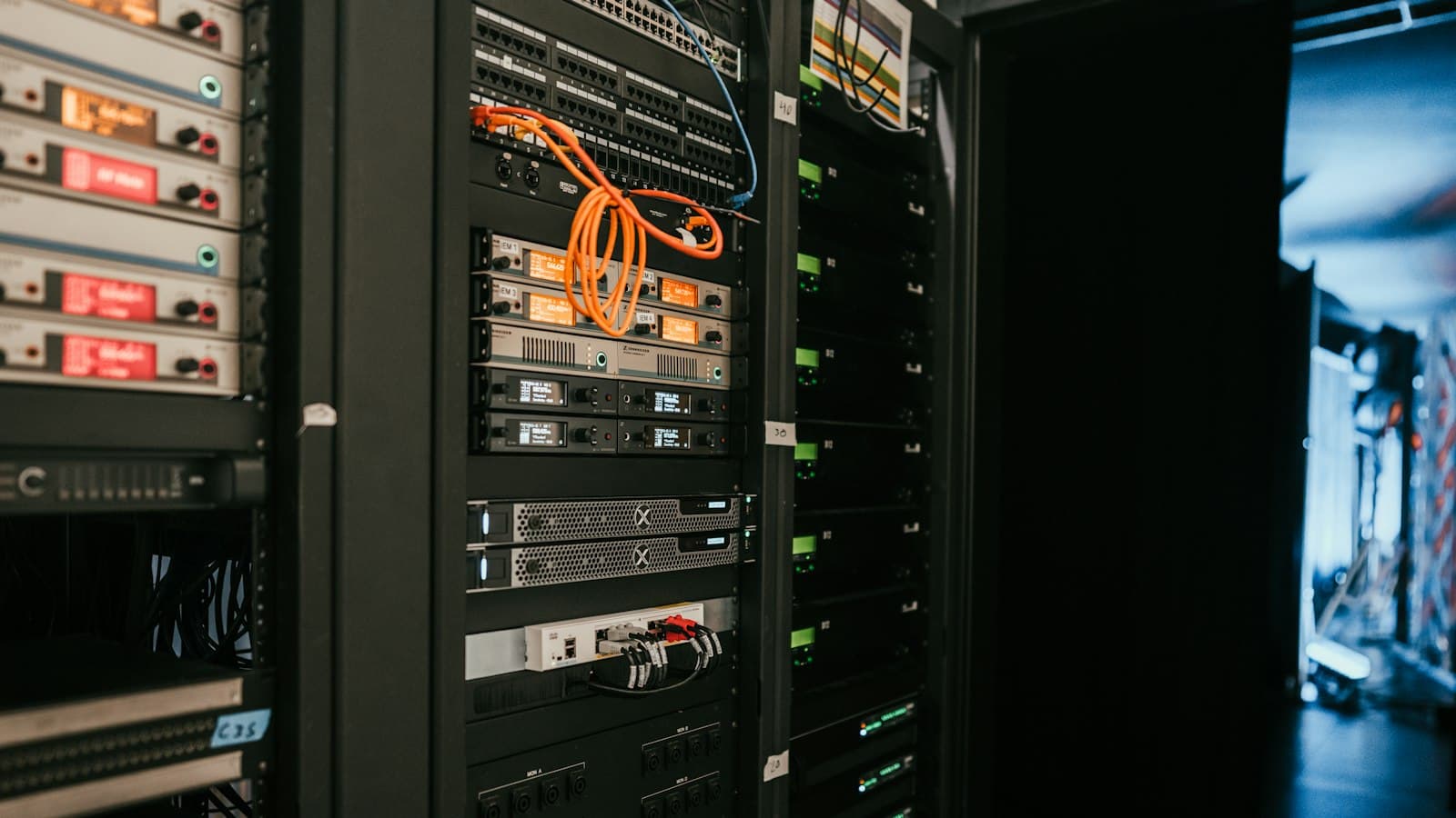 Rack-mounted servers and network equipment with orange and blue cables in a dim equipment room