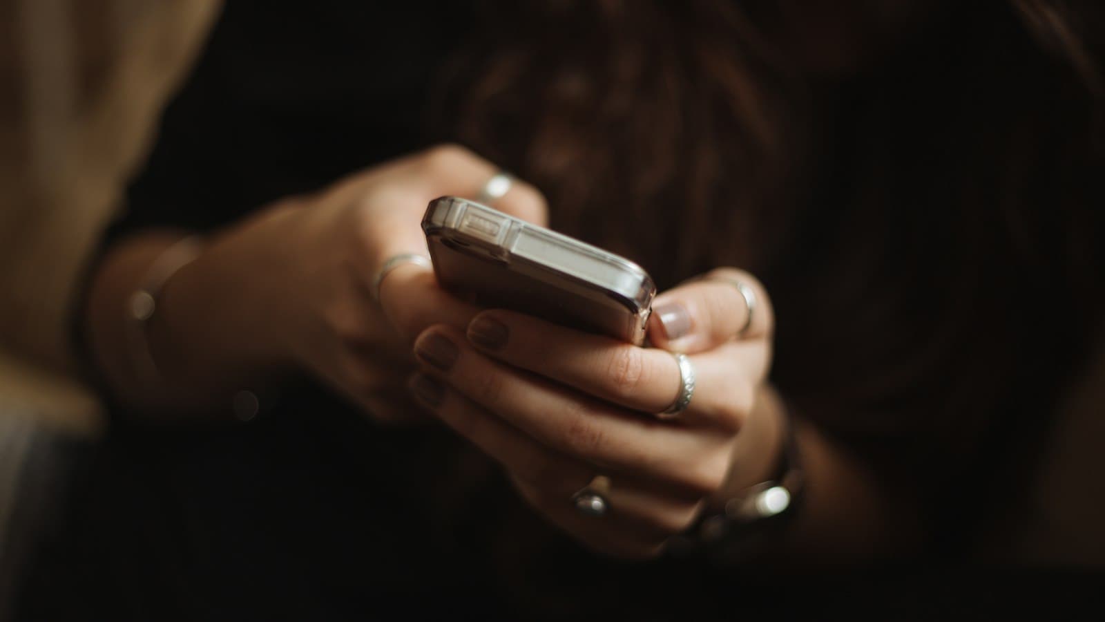 Two hands holding a smartphone in low light, thumbs resting on the screen