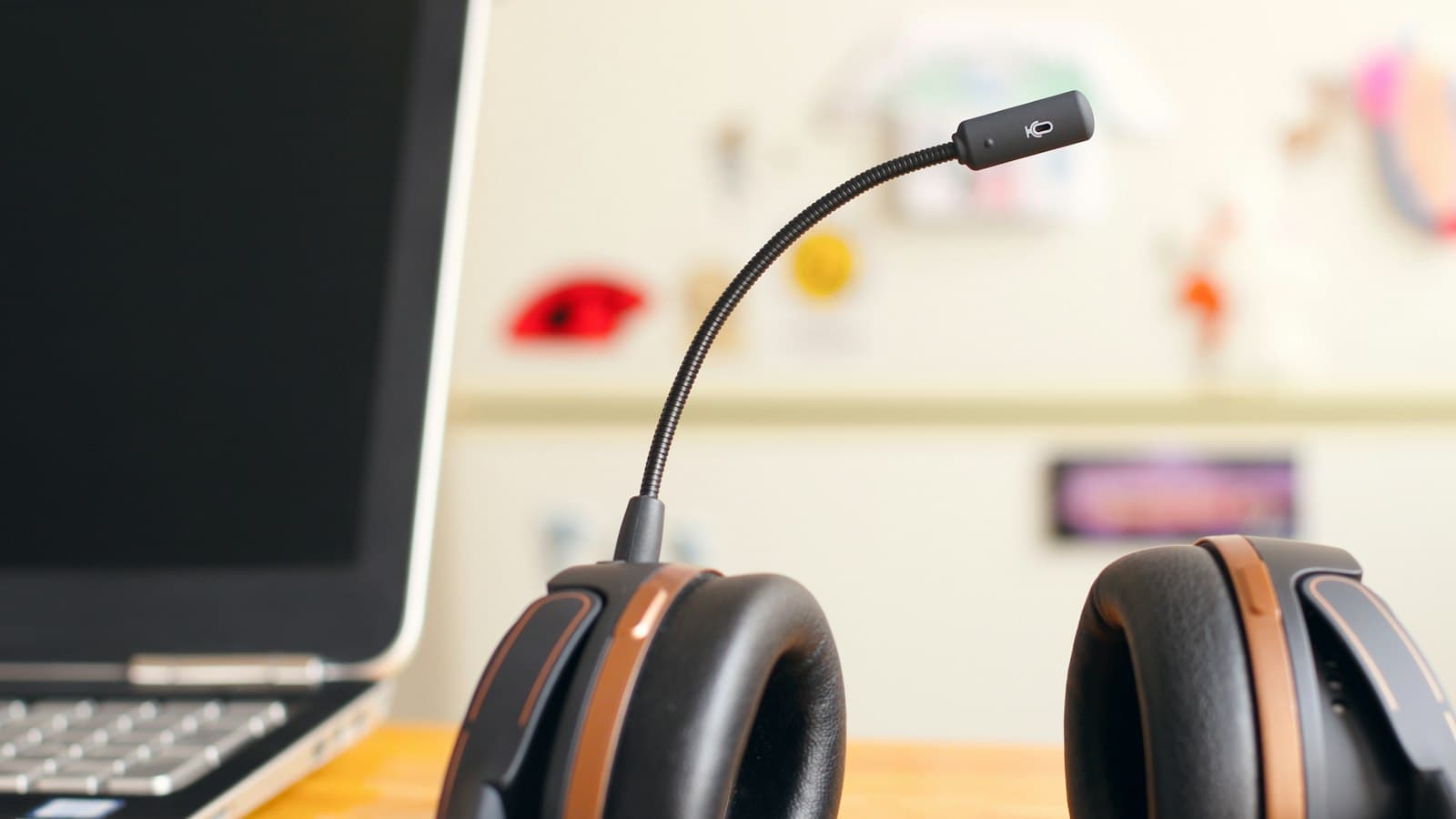 A black and copper headset with a boom microphone resting on a desk beside an open laptop