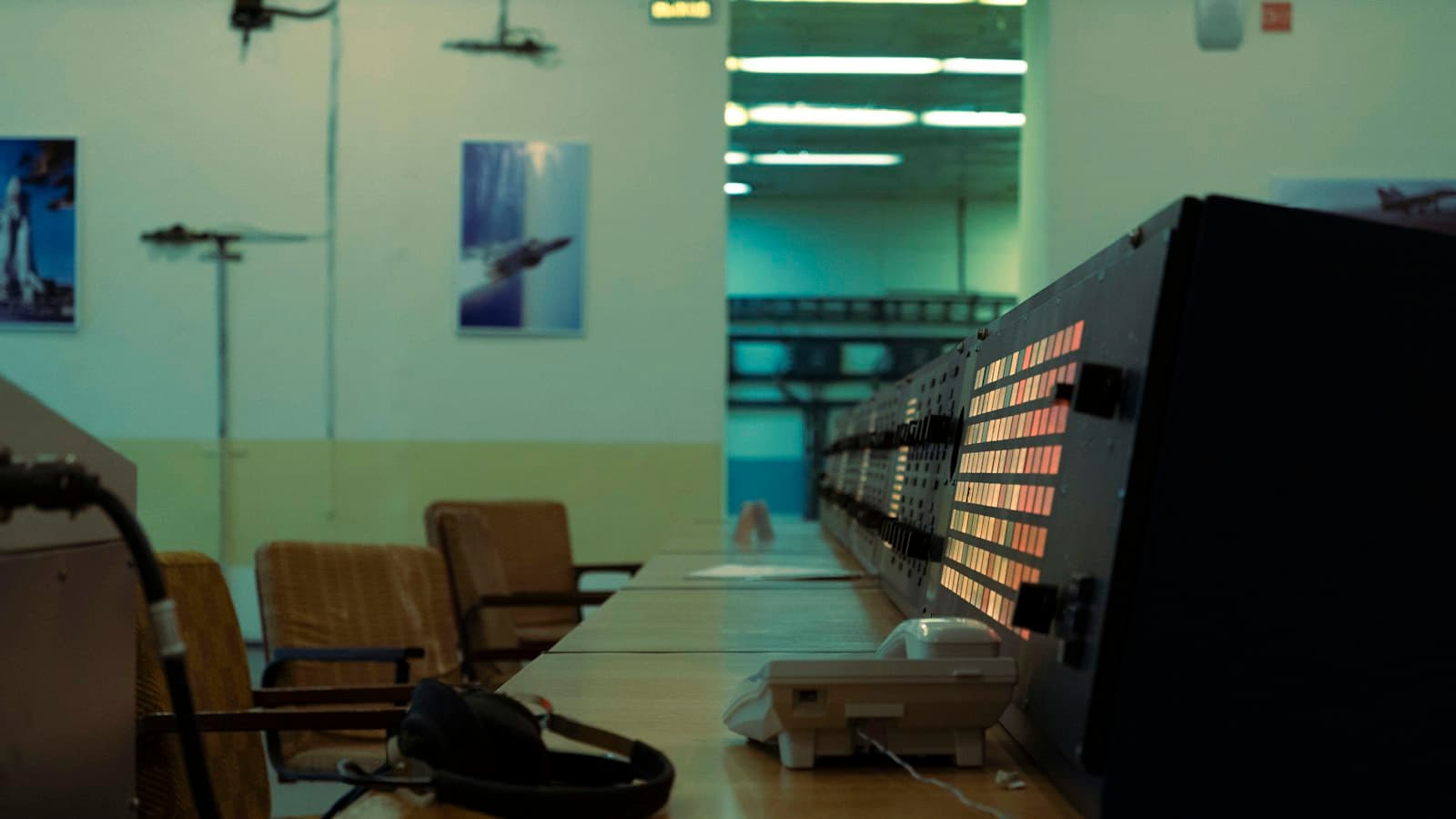 An empty control room with a long desk, headphones, a telephone and a console of indicator lights