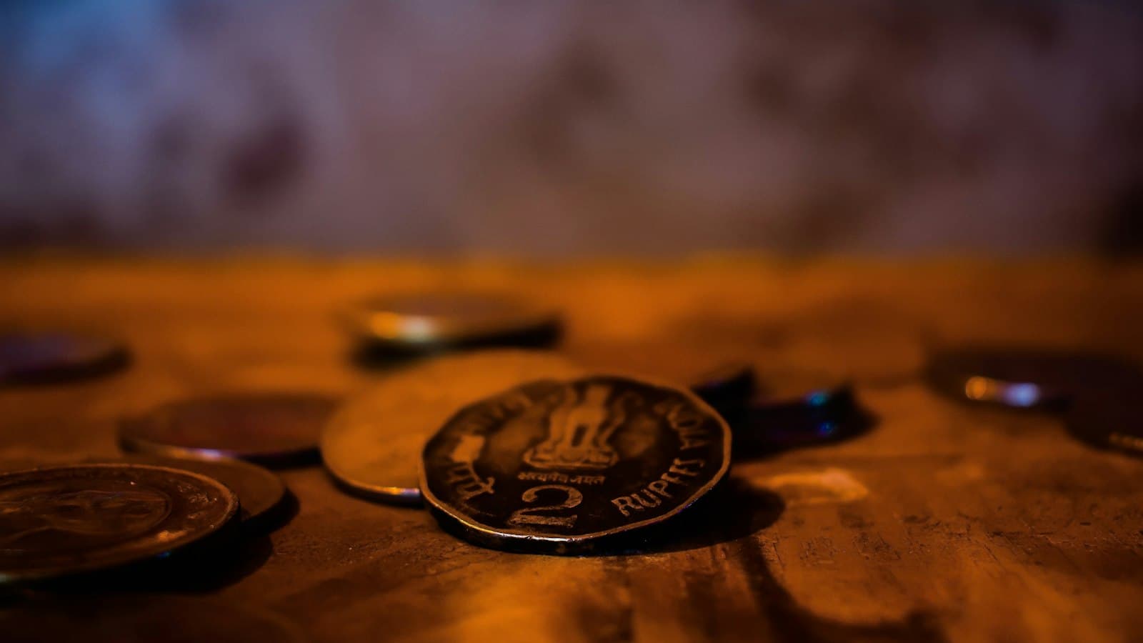 Close-up of Indian rupee coins on a wooden table, with a two rupee coin in sharp focus