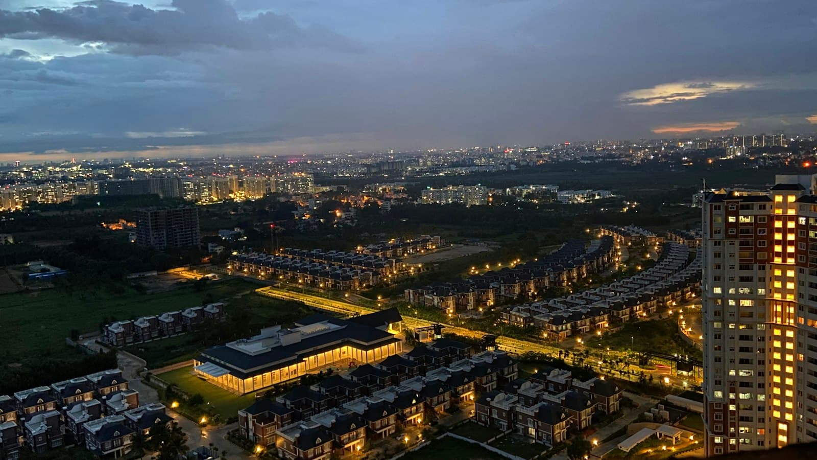 Aerial view of a city at dusk with lit apartment towers, rows of houses and a cloudy sky