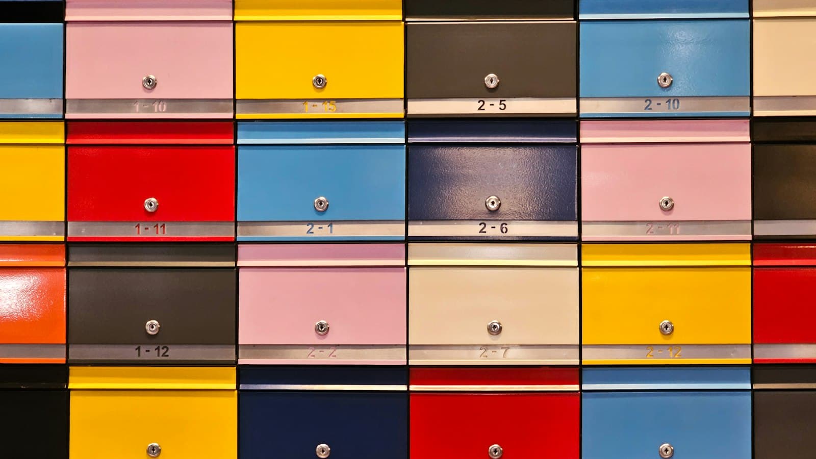 A wall of numbered metal mailboxes in yellow, red, blue, pink and grey, each with its own lock