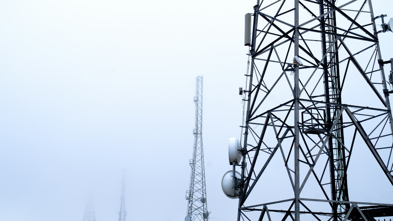 Steel telecom towers with microwave dishes fading into thick fog